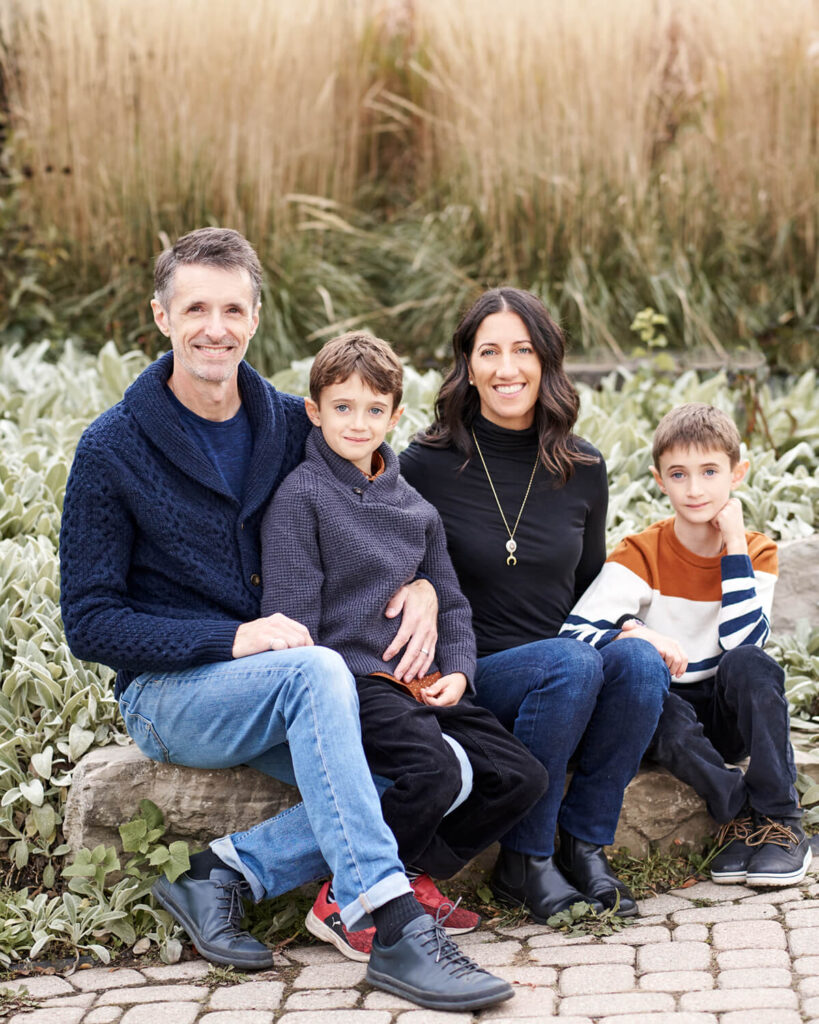 A family of four sits outdoors on a stone bench in a garden