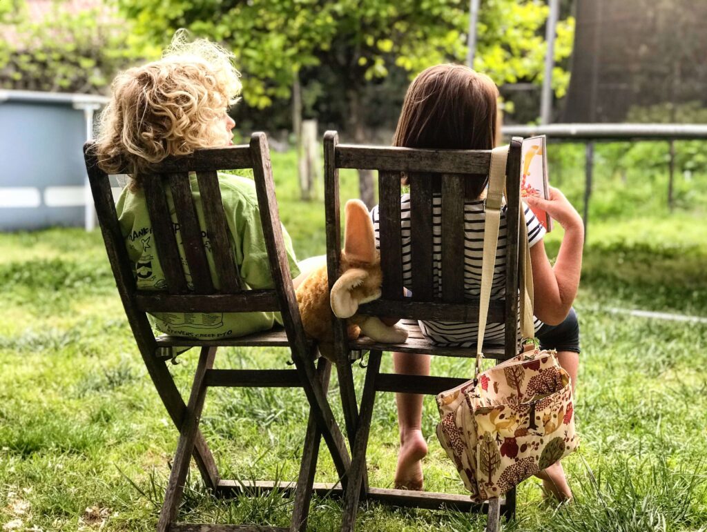 children sitting on wooden chairs outside