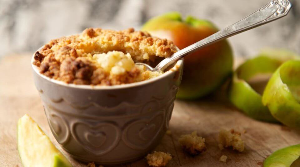 Apple crisp on a wood platter surrounded by fresh apples