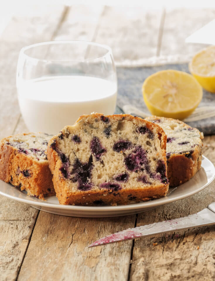 Lemon and blueberry loaf on a wooden table with a glass of milk