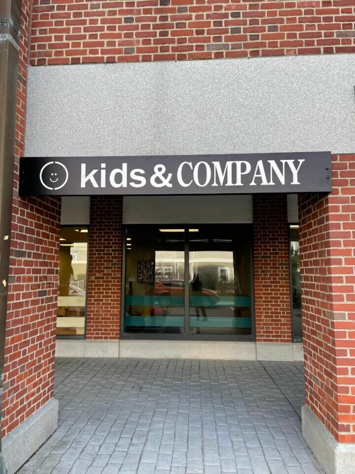 Entrance of a brick building featuring a sign that reads "kids & COMPANY" above glass doors.