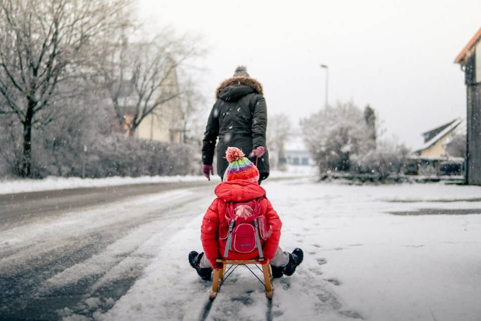 Child getting pulled on a toboggin by their parent