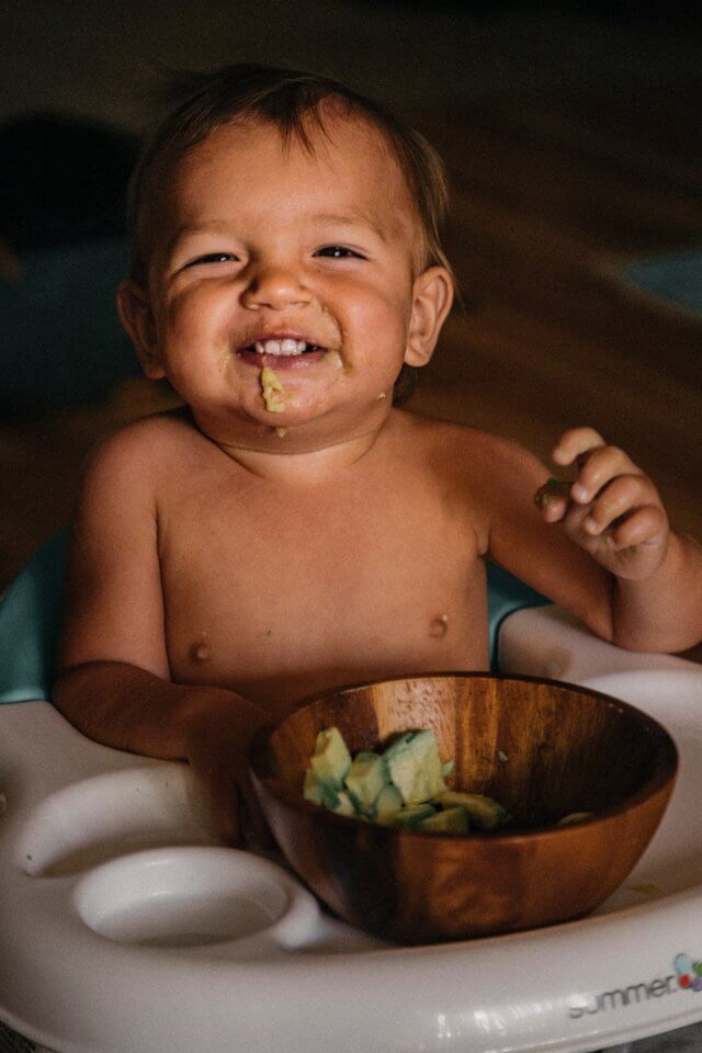 Baby eating avocado out of a brown bowl
