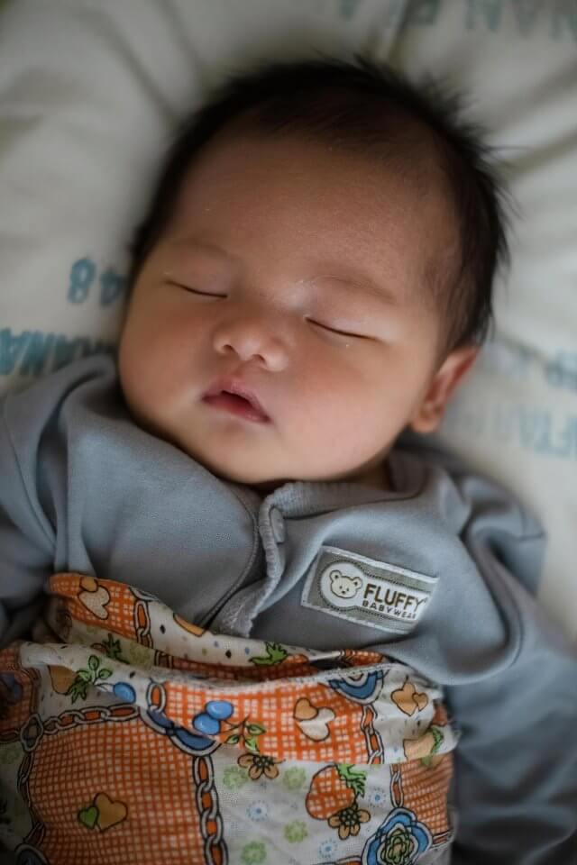 Baby sleeping in a grey outfit and orange blanket