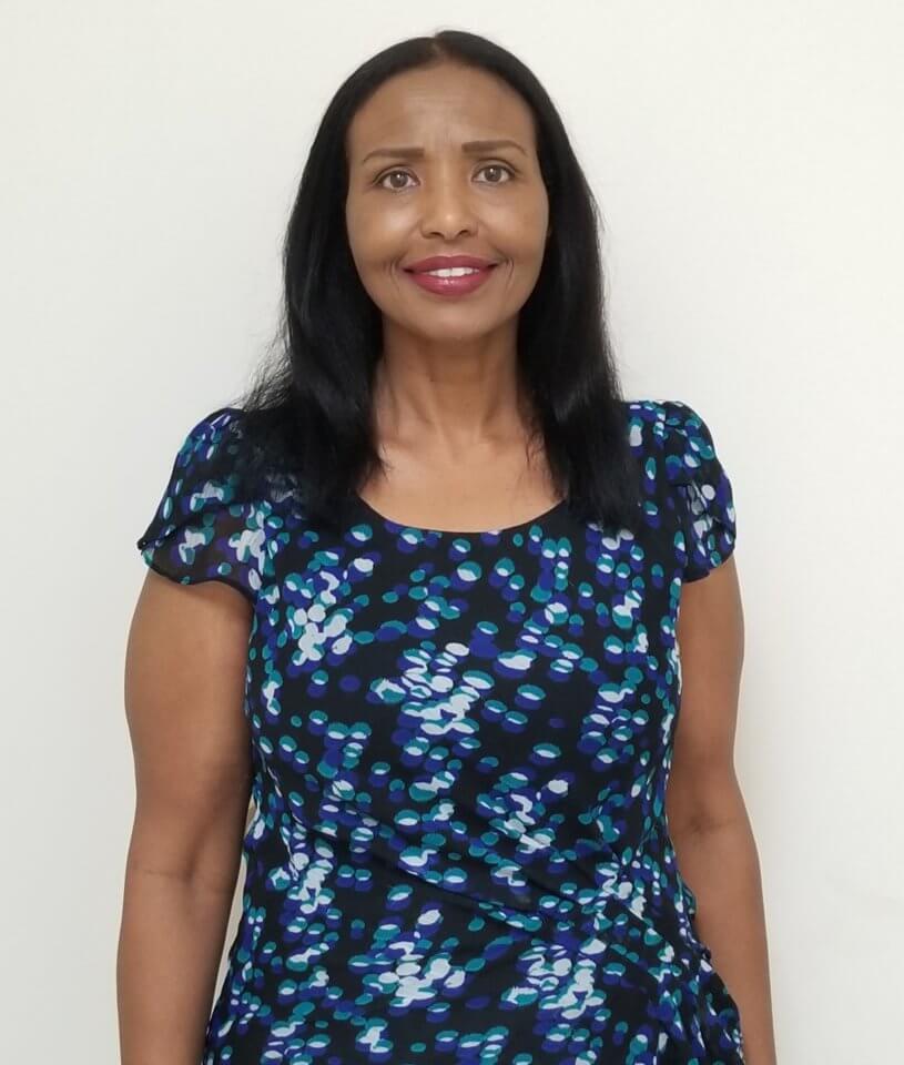 A woman with long black hair is standing against a plain white background, wearing a black dress with blue and white abstract patterns.