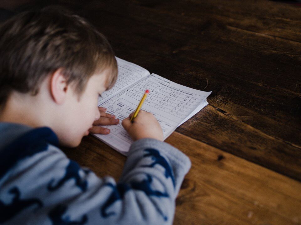 Child doing school work from home on a wooden table.