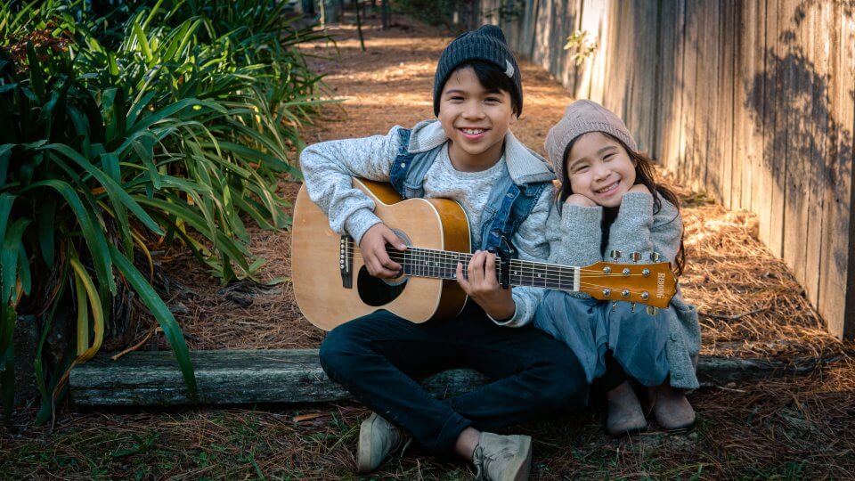 Children sitting down playing with a guitar.