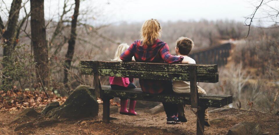 Family of three sitting on a bench in fall.