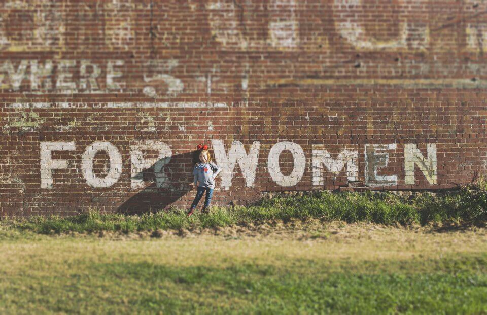 Little girl standing in front of a for women wall