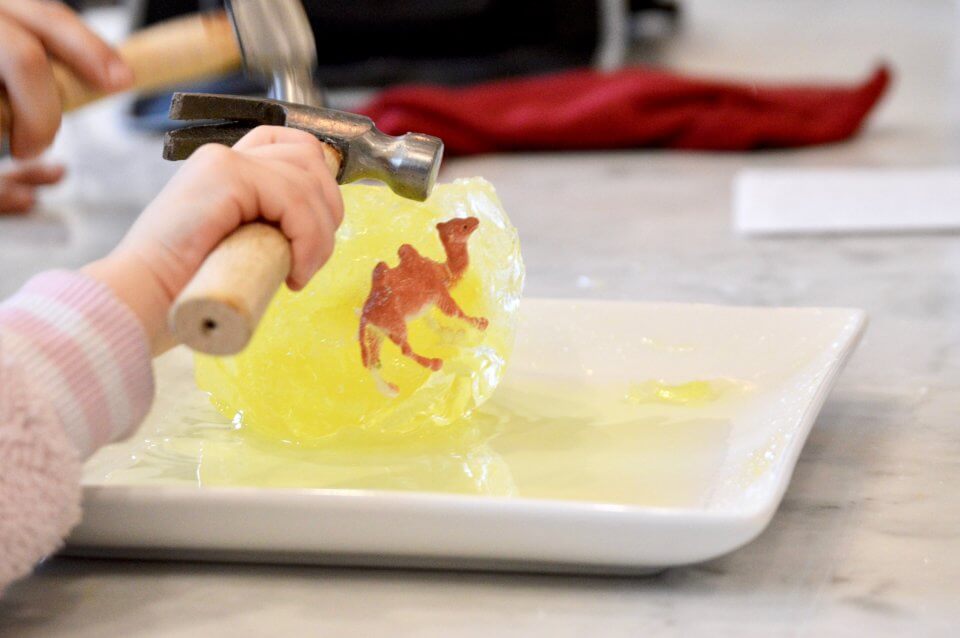 A child is using a hammer to get inside of dinosaur eggs.