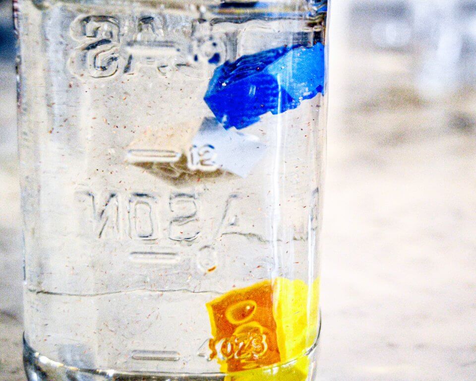 Photo of a glass jar filled with hair gel, warm water, glitter and floating Lego bricks. 