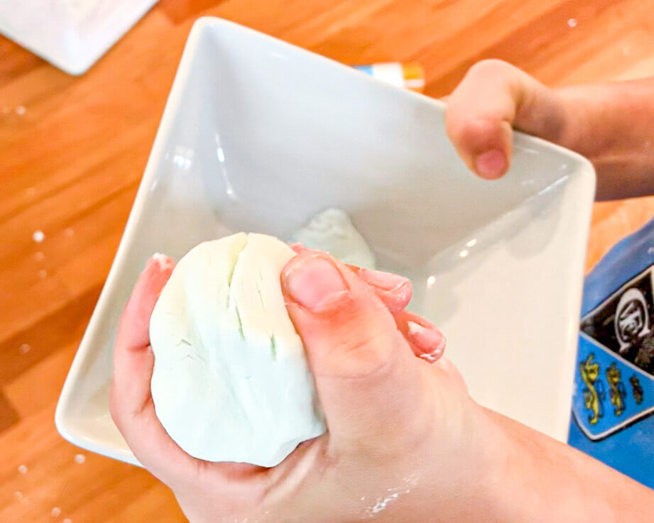 A child holding a dough ball in his hand, forming into the shape of a ball.