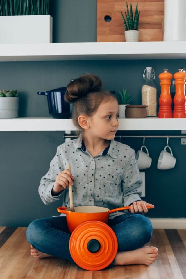 Child sitting on the floor eating food out of an orange pot