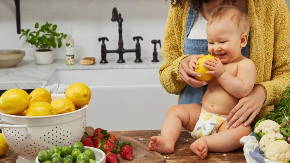 Baby sitting on the kitchen counter holding a lemon