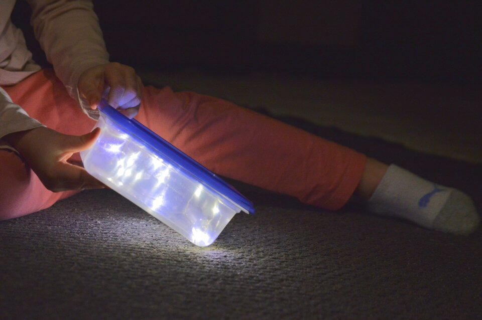 Child playing with lights in a tupperware container.