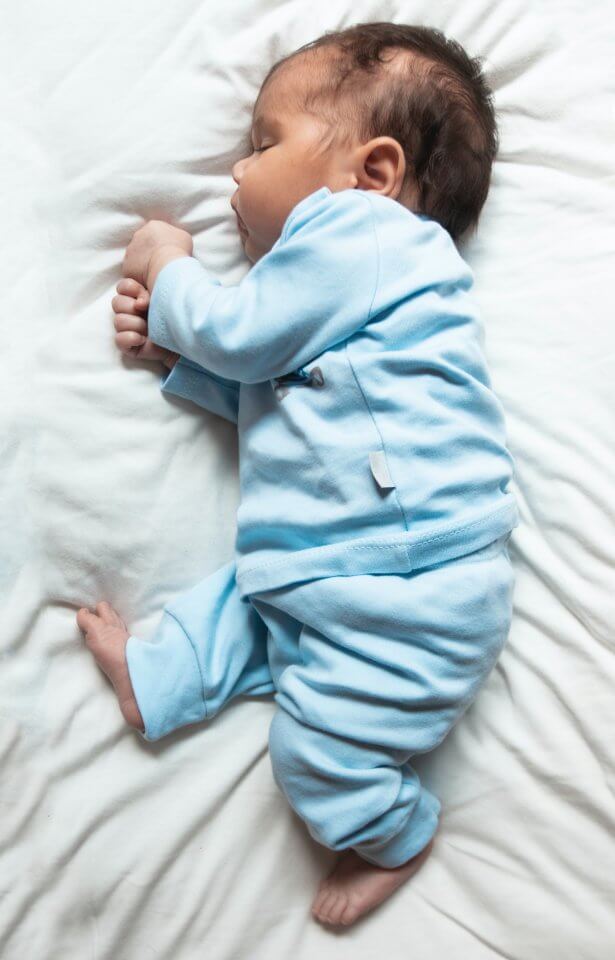 Newborn baby in blue outfit on a white bed