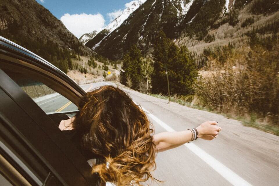 Road trip - woman with her head out of the car in the mountains