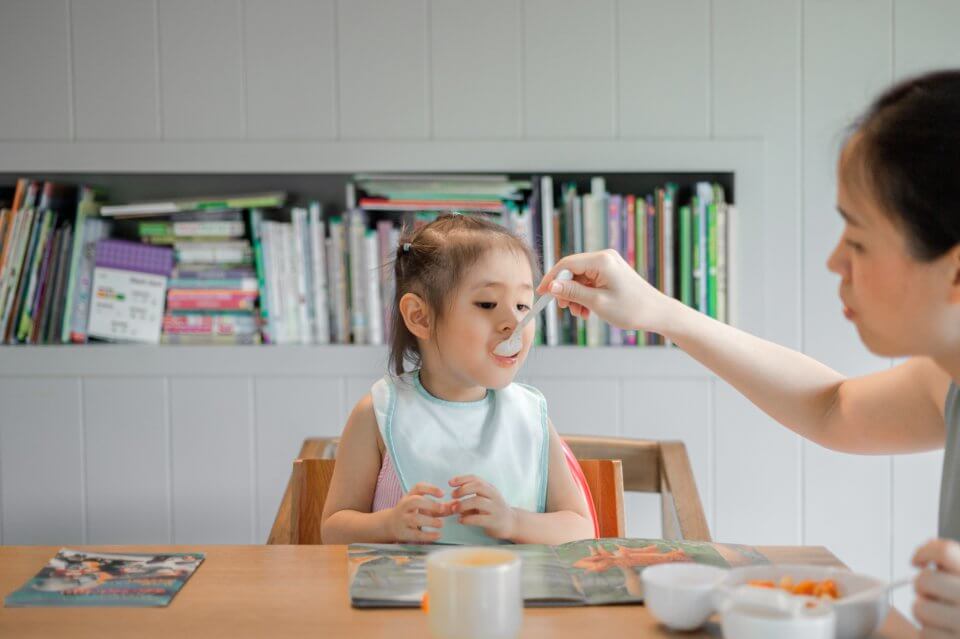 Child being fed by a spoon by her mother