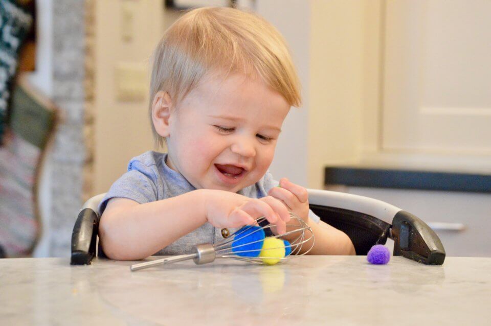 A child is playing with pom poms in a whisk, exploring his senses.