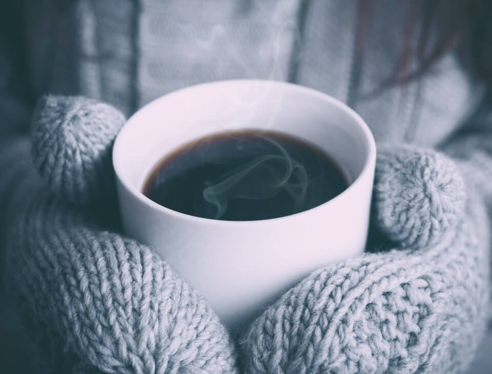 Grey winter mittens around around a warm cup of coffee. 